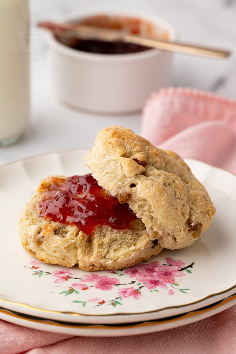 Fruit Scones Freshly baked Fruit Scone split open and topped with glossy strawberry jam, served on a floral vintage plate.