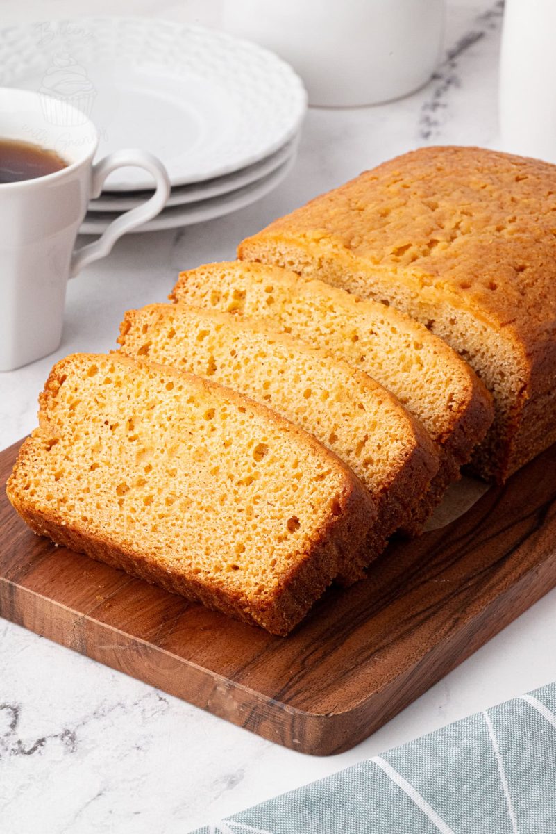 Golden Syrup Cake Sliced loaf of golden syrup cake on a wooden board with coffee cups in the background.
