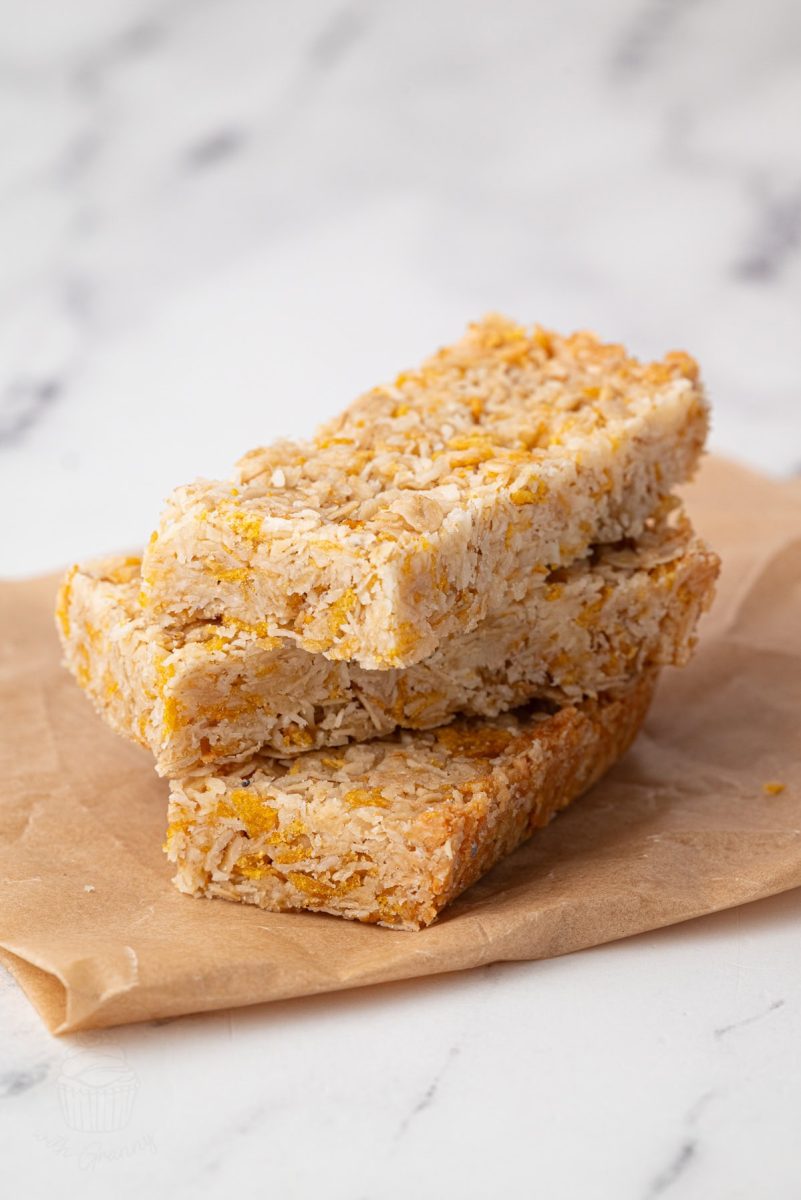 Honey Slice Three honey slice bars stacked on brown parchment paper, showing golden oat texture and neat edges.
