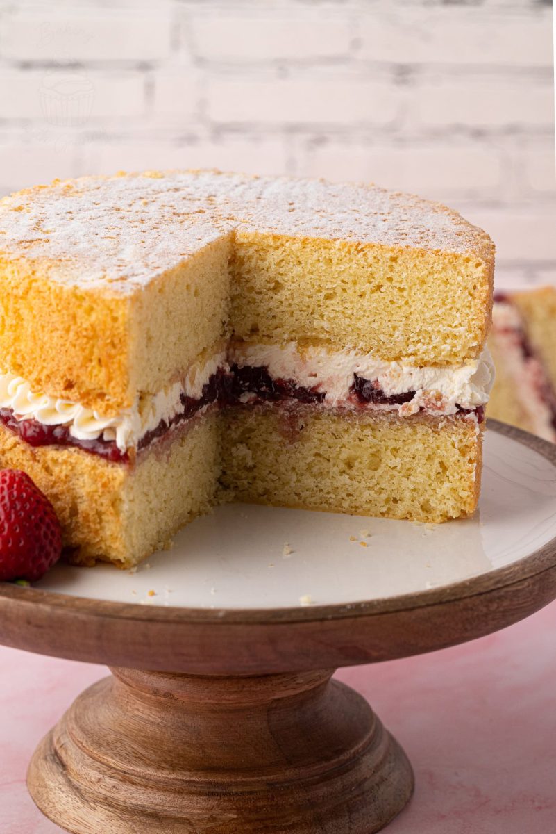 Victoria Sponge Close-up of a classic Victoria Sponge cake on a wooden cake stand, dusted with caster sugar and filled with strawberry jam and buttercream.